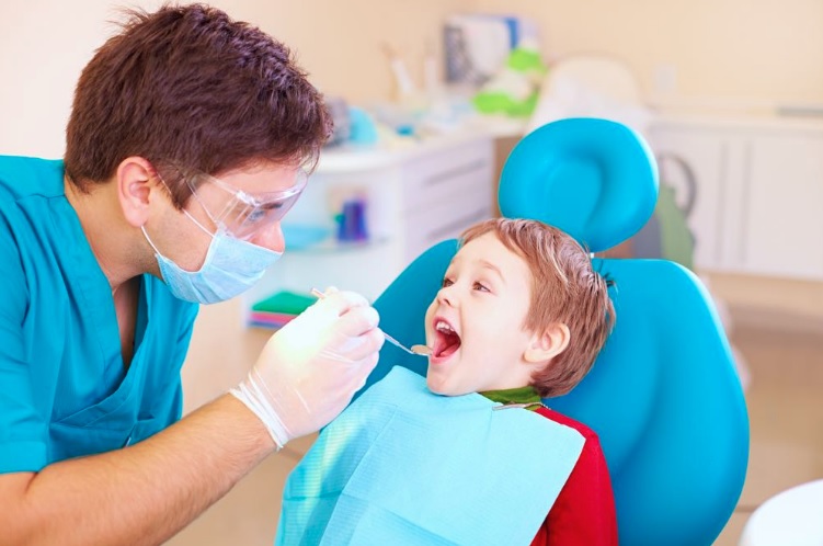 Children's dentist examining a young child's teeth in the dental chair